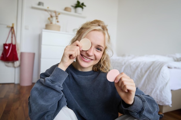 Free photo portrait of young woman chatting on live stream about makeup sits on floor in bedroom showing beauty