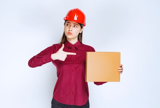 Portrait of a young woman in crash helmet pointing at small paper box . 