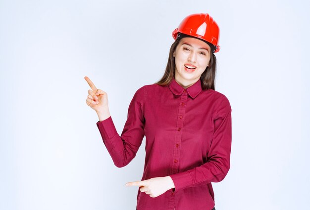 Portrait of young woman in crash helmet pointing up. 