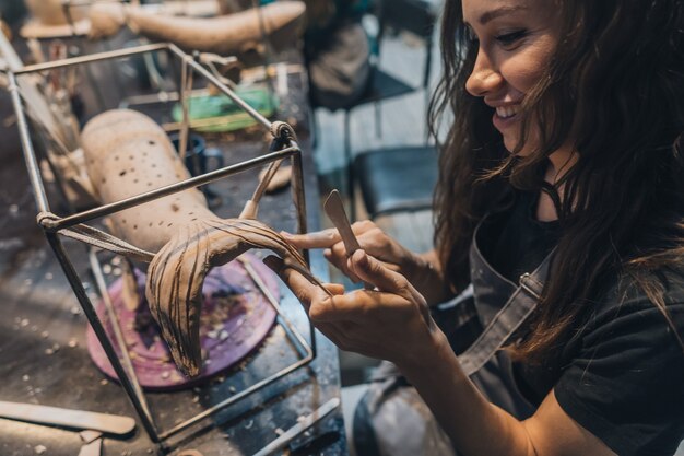 Portrait of young woman enjoying favorite job in workshop. The potter carefully works on the clay whale