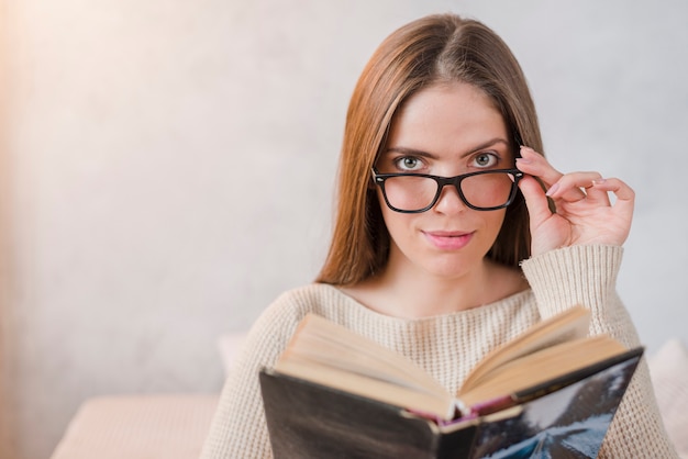 Free photo portrait of young woman fixed eyeglasses to read book