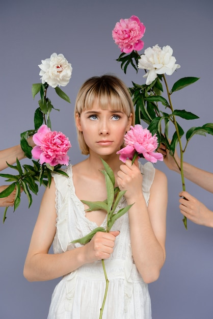 Portrait of young woman among flowers over grey wall