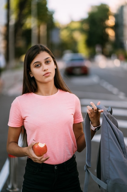 Free Photo portrait of a young woman holding apple against a street background