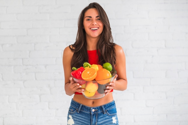 Portrait of young woman holding bowl of fresh vegetables and fruits