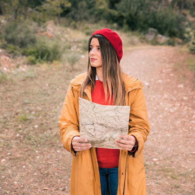 Free photo portrait of a young woman holding map in hand standing on trail