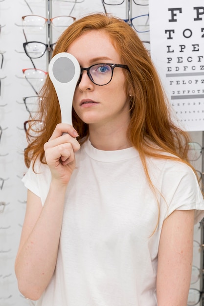 Portrait of young woman holding optics occluder in front of her eye