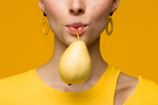 Portrait of young woman holding pear in her mouth