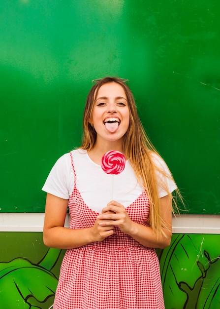 Free photo portrait of a young woman holding red lollipop in hand showing her tongue