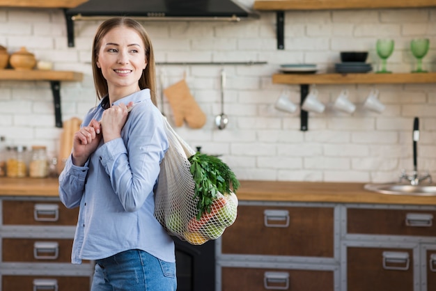 Portrait of young woman holding reusable bag with groceries