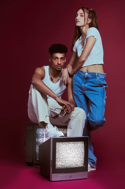 Free photo portrait of young woman and man in 2000s fashion style posing together with tv