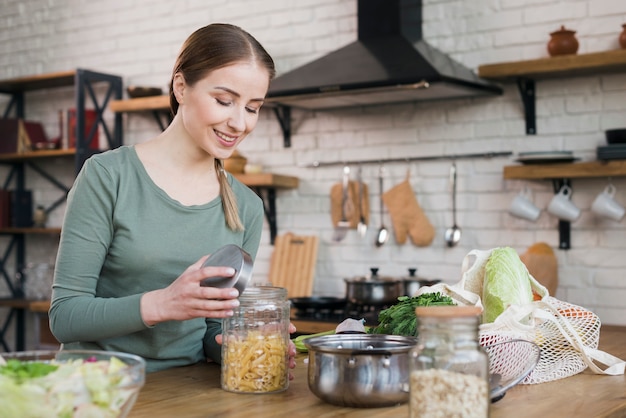 Free photo portrait of young woman opening jar with organic pasta