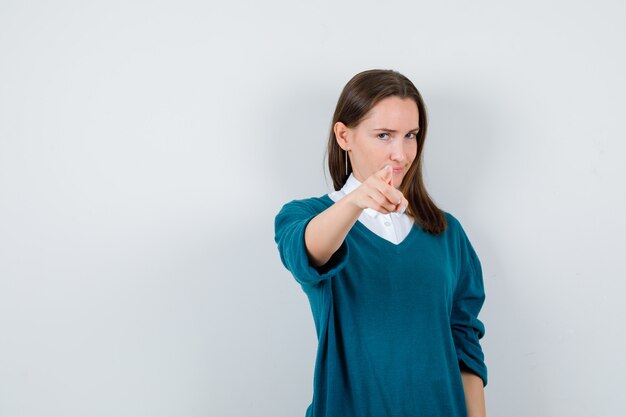 Portrait of young woman pointing forward in sweater over white shirt and looking sensible front view