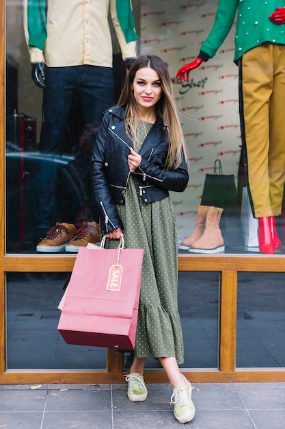 Portrait of a young woman posing in front of window display holding shopping bags in hand