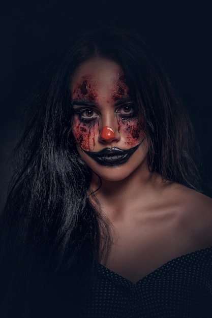 Free photo portrait of young woman in a role of evil scary clown at dark photo studio.