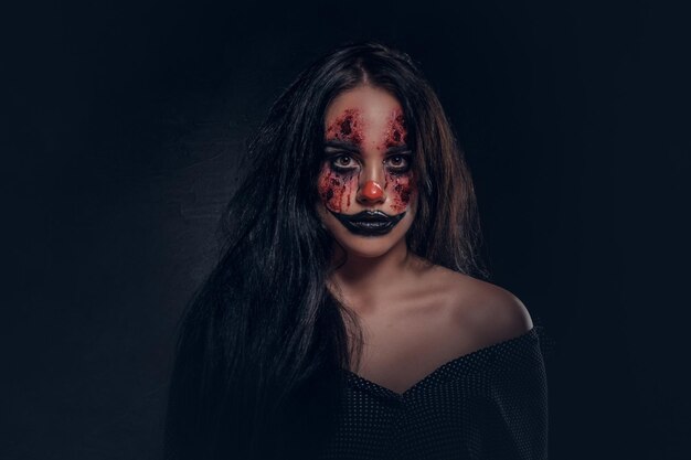 Portrait of young woman in a role of evil scary clown at dark photo studio.