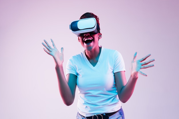 Portrait of young woman's playing in VR-glasses in neon light on gradient