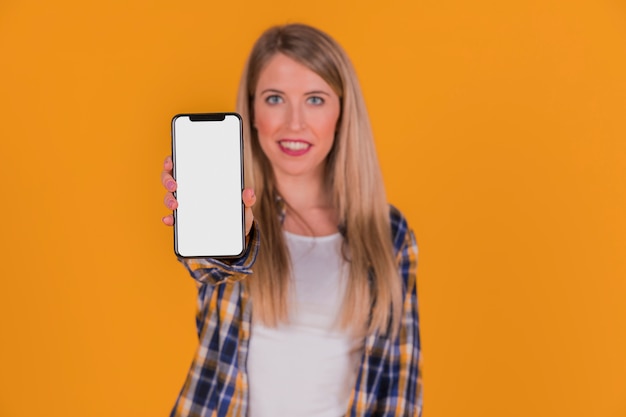 Free photo portrait of a young woman showing her mobile phone against orange background