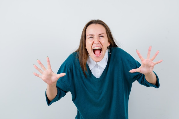 Free photo portrait of young woman showing open hands while screaming in sweater over white shirt and looking aggressive front view