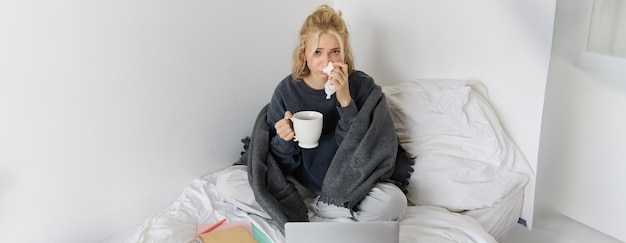 Free photo portrait of young woman sitting at home sick feeling unwell drinking tea spending time in bed has