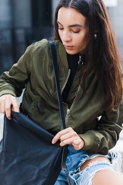 Portrait of a young woman sitting outside looking in the bag