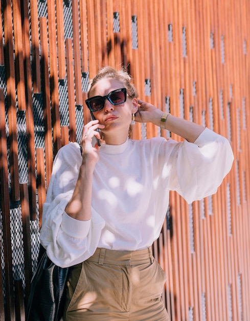 Free photo portrait of a young woman standing against wall talking on cellphone