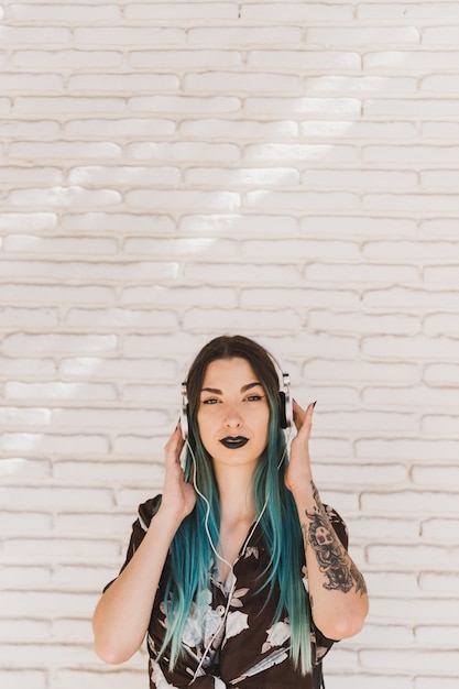 Free Photo portrait of a young woman standing in front of wall listening music on headphone