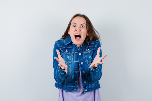 Free Photo portrait of young woman stretching hands at front while screaming in denim jacket and looking aggressive front view