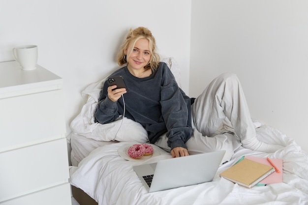 Free Photo portrait of young woman student studying in her bed relaxing while preparing homework eating