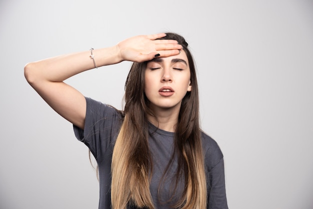 Portrait of young woman touching her forehead posing over gray background.