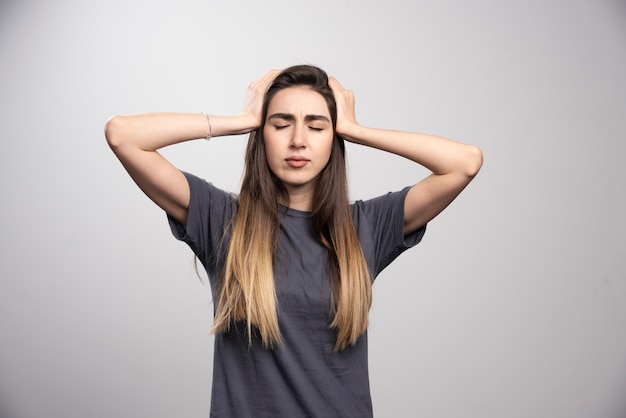 Portrait of young woman touching her head posing over gray background.