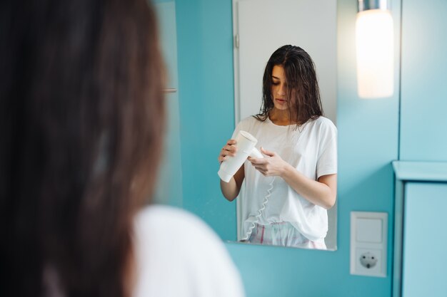 Portrait of young woman using hairdryer in bathroom