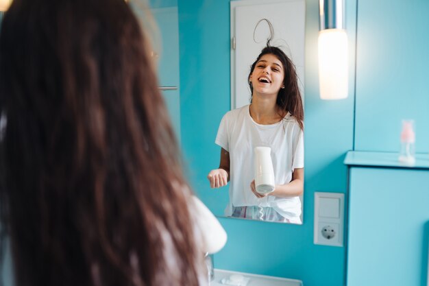 Portrait of young woman using hairdryer in bathroom.