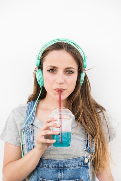 Free photo portrait of young woman wearing headphone drinking juice with straw