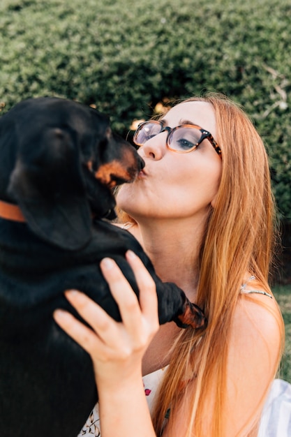 Portrait of a young woman wearing spectacles kissing her dog