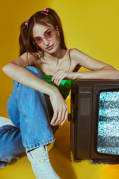 Free photo portrait of young woman with 2000s fashion style posing with tv