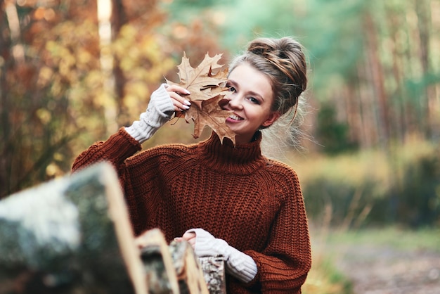 Free photo portrait of young woman with autumnal leaves in forest