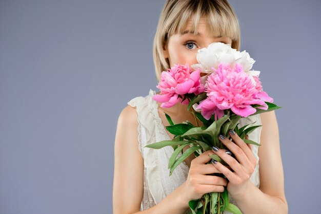 Portrait of young woman with bouquet flowers over grey backgro