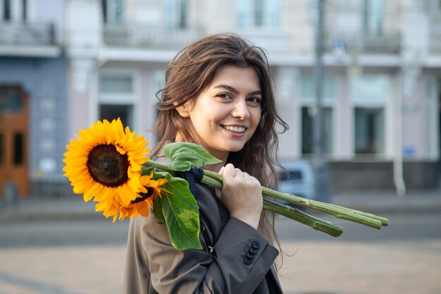 Portrait of a young woman with a bouquet of sunflowers in the city