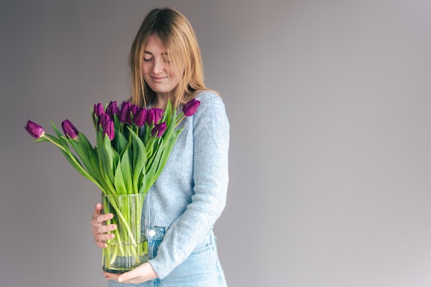 Portrait of a young woman with a bouquet of tulips on a gray background