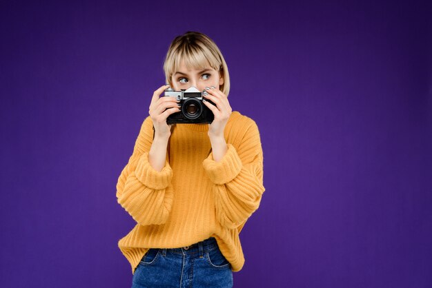 Portrait of young woman with camera over purple wall