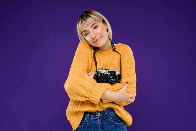 Free photo portrait of young woman with camera over purple wall