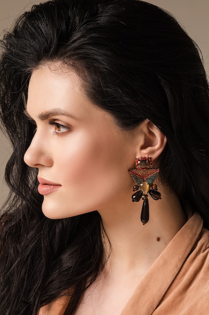 Portrait of young woman with healthy skin and earrings on her ears isolated on wall