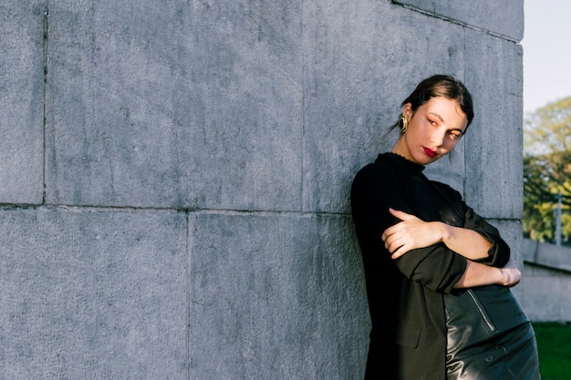 Portrait of a young woman with her arms crossed standing against wall