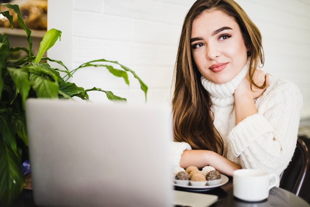 Portrait of a young woman with laptop; coffee and chocolate truffles on table