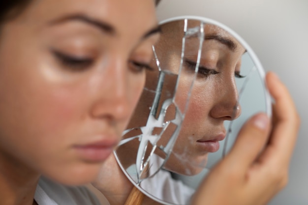 Free Photo portrait of young woman with low self-esteem looking in a hand-held mirror