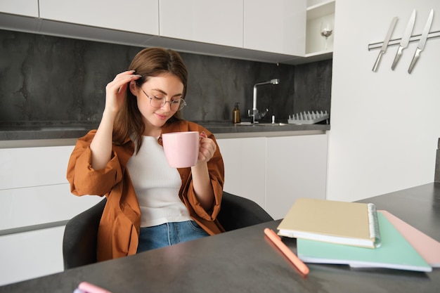 Free Photo portrait of young woman working from home taking a break for cup of tea girl studies remotely sits