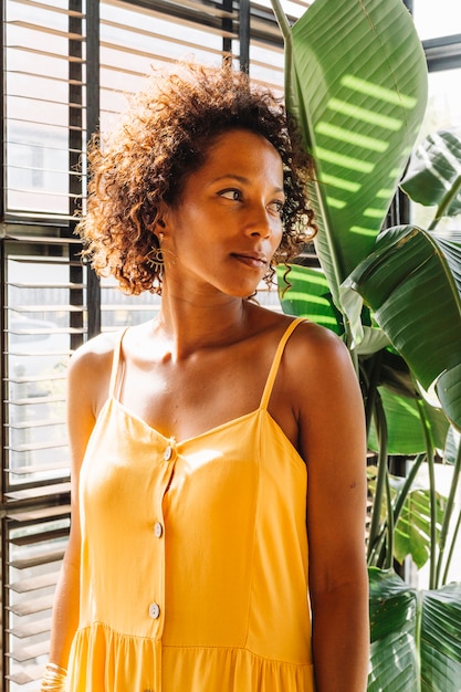 Free photo portrait of young woman in yellow dress standing near the window