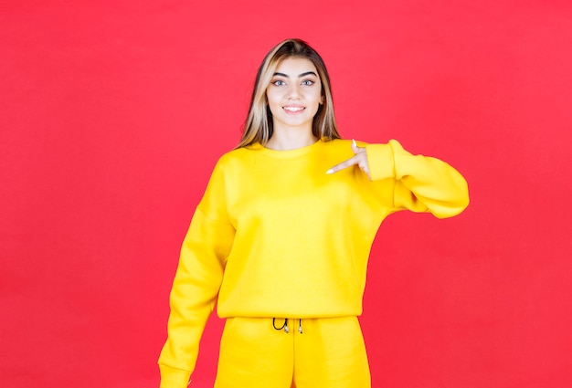 Free photo portrait of young woman in yellow outfit pointing at somewhere