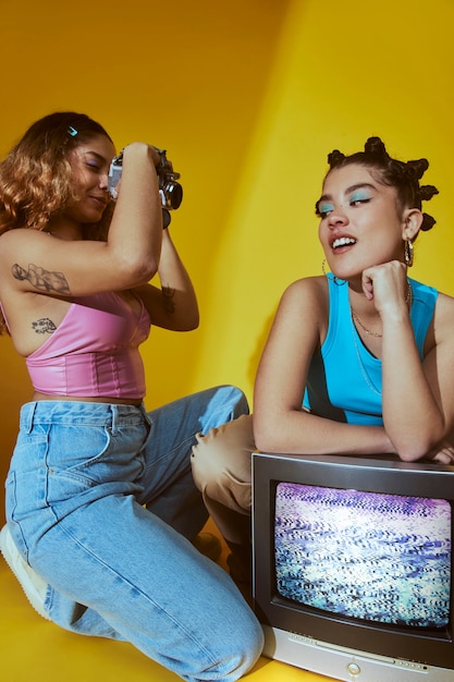 Portrait of young women in 2000s fashion style posing with tv and camera