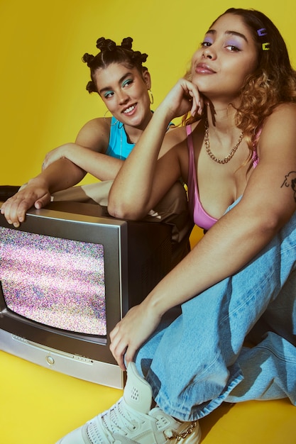 Free photo portrait of young women in 2000s fashion style posing with tv